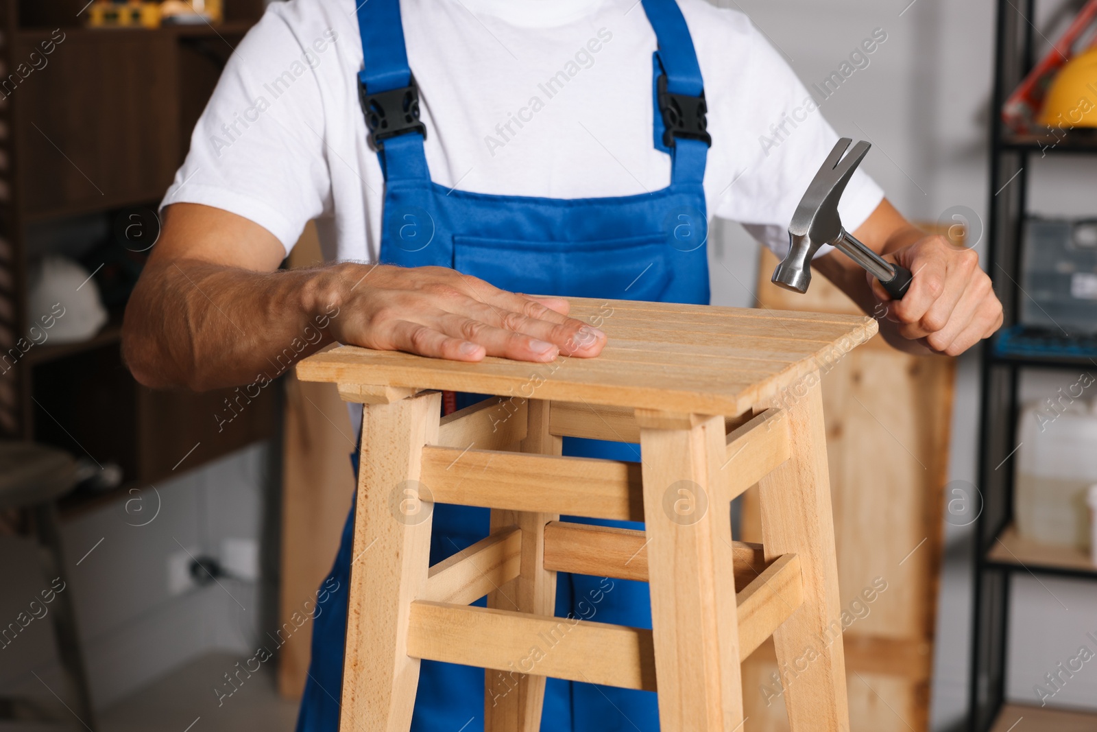 Photo of Man repairing wooden stool with hammer indoors, closeup