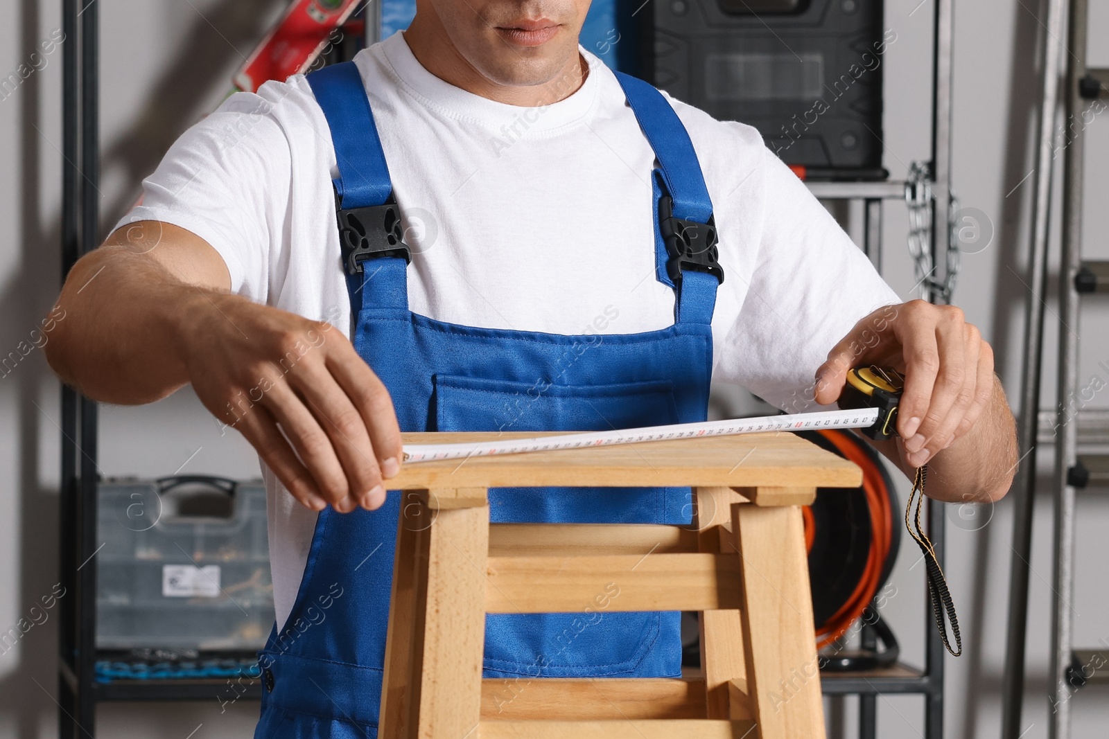 Photo of Man using tape measure while repairing wooden stool indoors, closeup