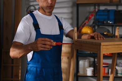 Man repairing wooden stool with screwdriver indoors, closeup