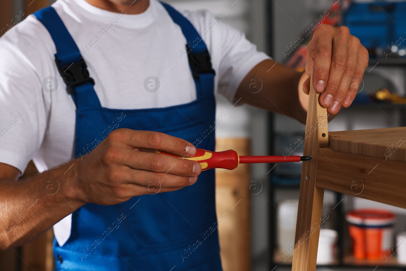 Photo of Man repairing wooden stool with screwdriver indoors, closeup