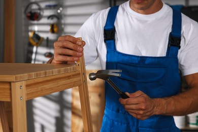 Photo of Man repairing wooden stool with hammer indoors, closeup