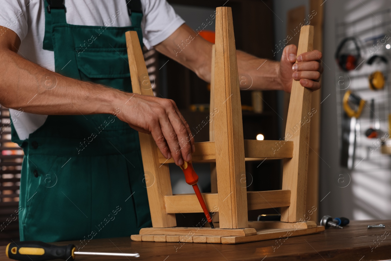 Photo of Man repairing wooden stool with screwdriver indoors, closeup