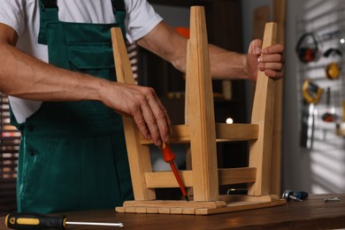 Man repairing wooden stool with screwdriver indoors, closeup