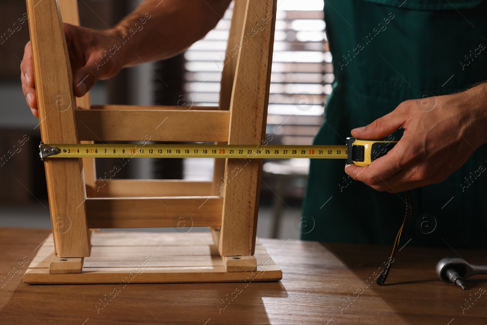 Photo of Man using tape measure while repairing wooden stool indoors, closeup