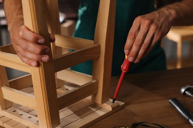 Man repairing wooden stool with screwdriver indoors, closeup