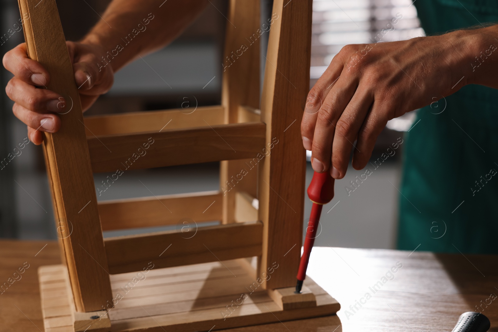 Photo of Man repairing wooden stool with screwdriver indoors, closeup