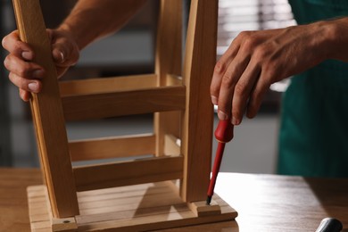 Photo of Man repairing wooden stool with screwdriver indoors, closeup