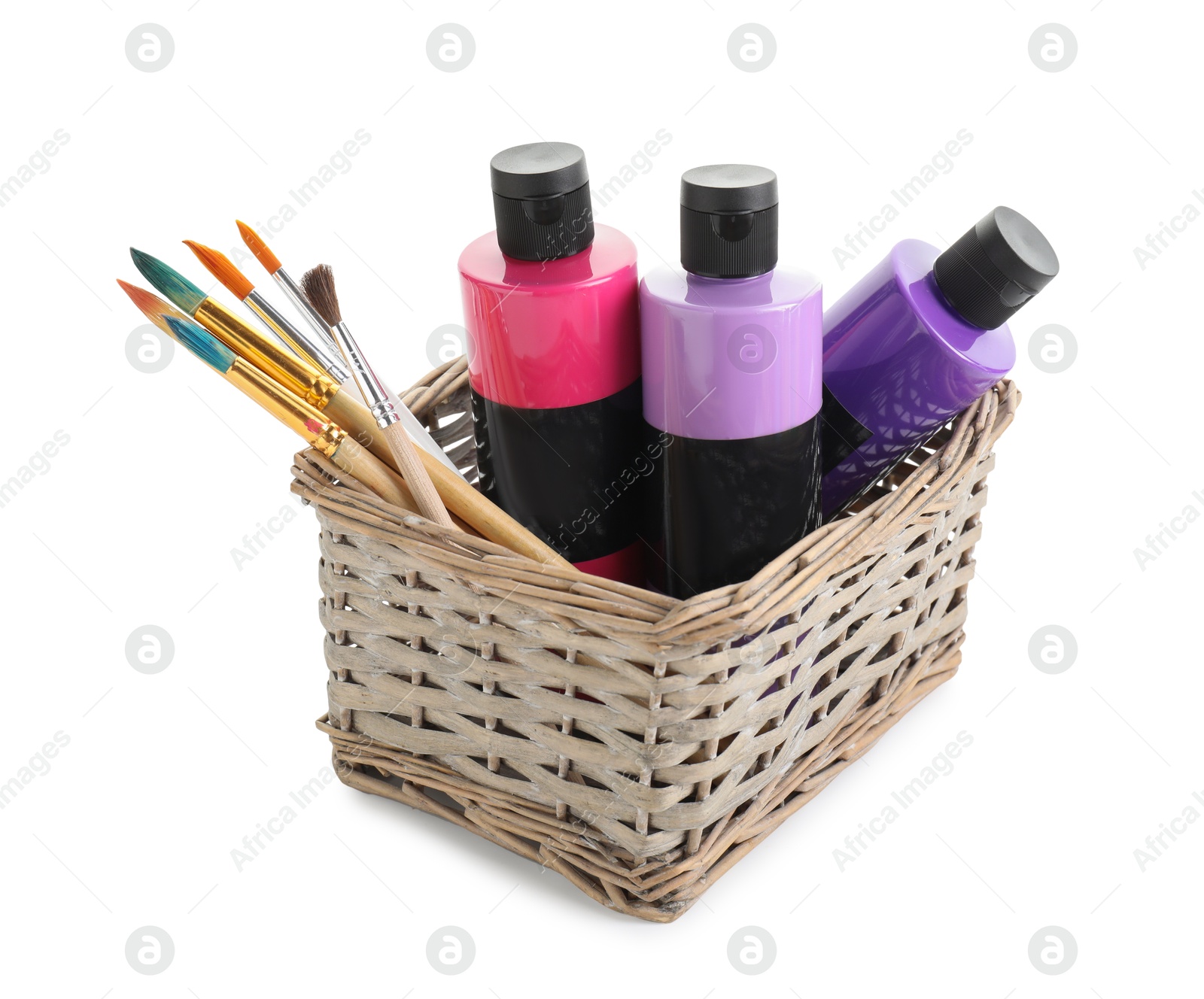 Photo of Acrylic paints of different colors and brushes in wicker basket isolated on white