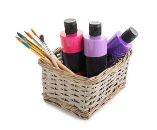 Photo of Acrylic paints of different colors and brushes in wicker basket isolated on white