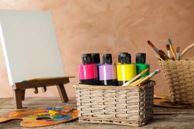 Photo of Acrylic paints of different colors, small easel, palette and brushes on wooden table