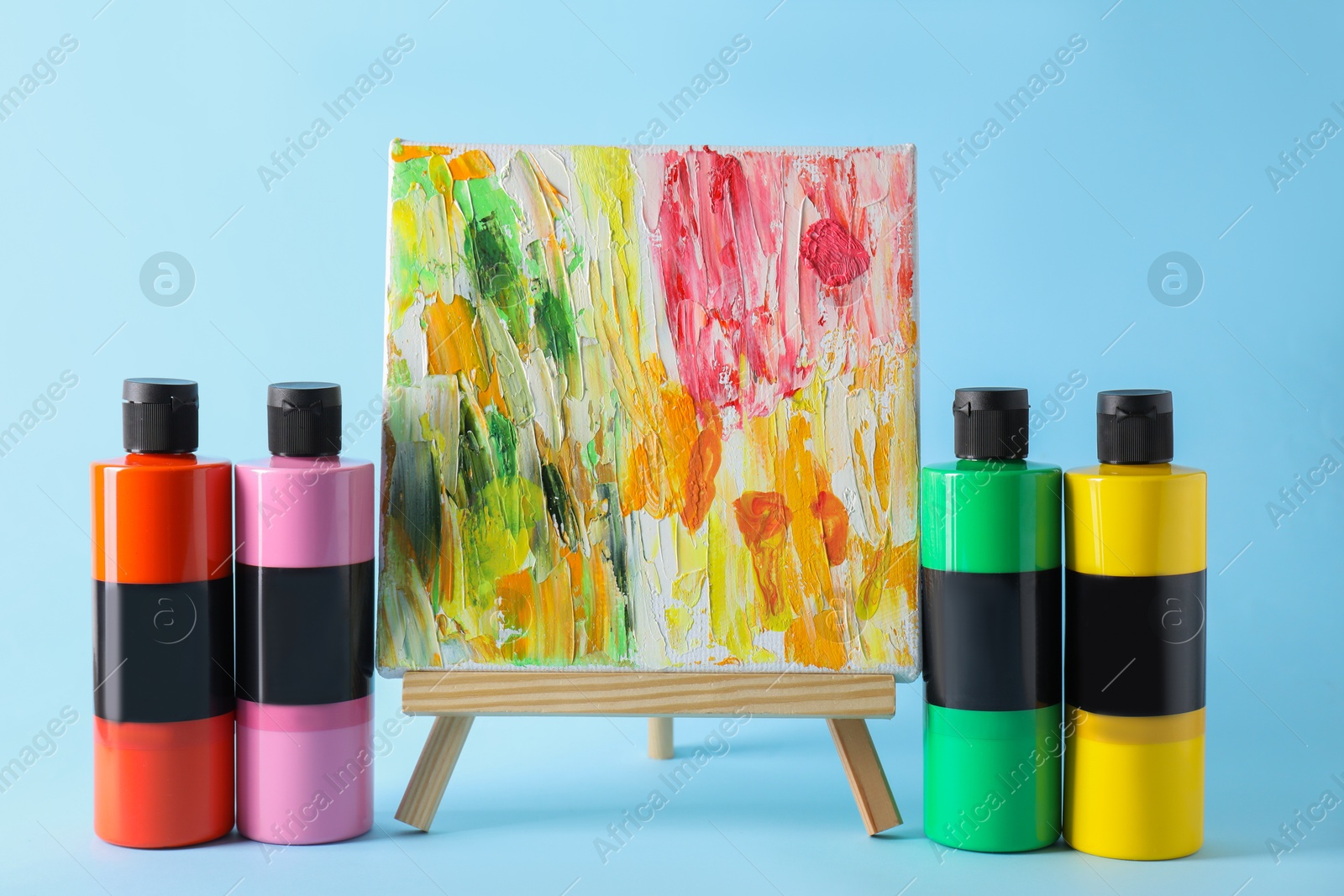 Photo of Acrylic paints of different colors and small easel with abstract picture on light blue background