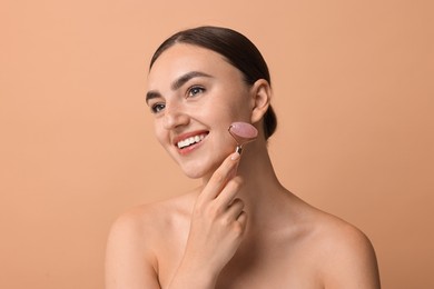 Beautiful young woman doing facial massage with roller on beige background