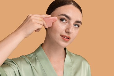 Beautiful young woman doing facial massage with gua sha tool on beige background