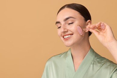 Beautiful young woman doing facial massage with roller on beige background, space for text