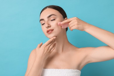 Photo of Beautiful young woman doing facial massage with gua sha tool on light blue background