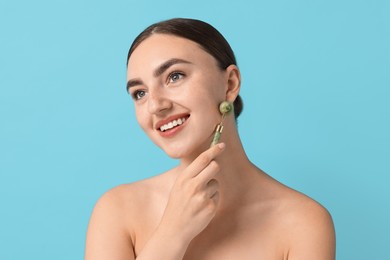 Beautiful young woman doing facial massage with roller on light blue background