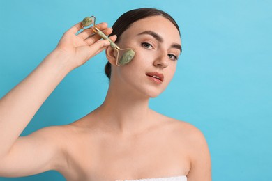 Photo of Beautiful young woman doing facial massage with roller on light blue background