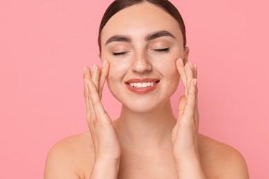 Beautiful young woman doing facial massage on pink background