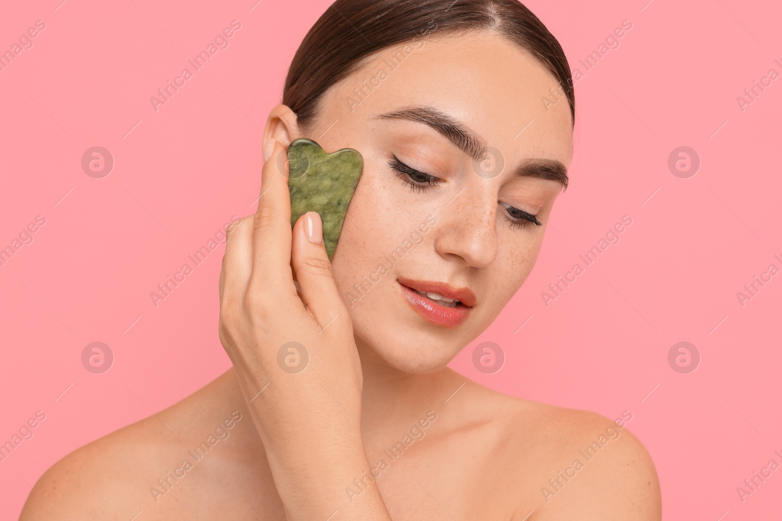 Photo of Beautiful young woman doing facial massage with gua sha tool on pink background