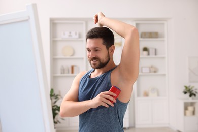 Photo of Smiling man applying solid deodorant at home