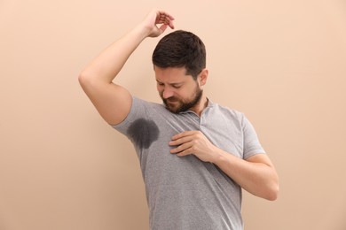 Man in t-shirt before using deodorant on beige background