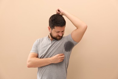 Man in t-shirt before using deodorant on beige background