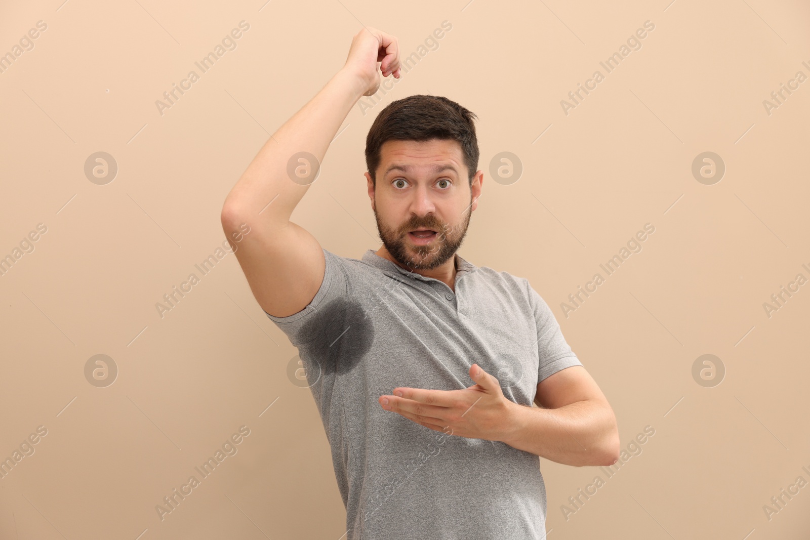 Photo of Emotional man in t-shirt before using deodorant on beige background