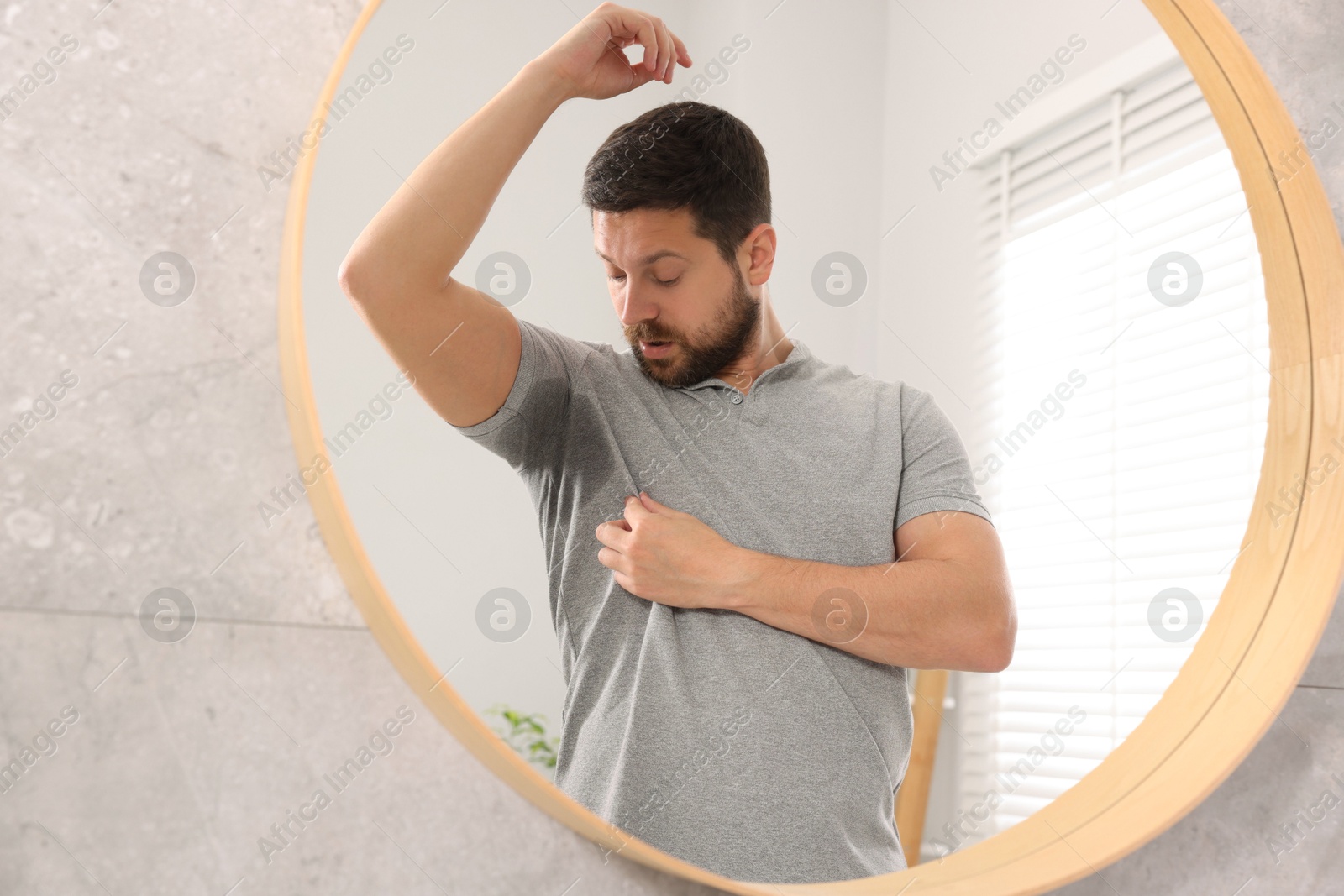 Photo of Emotional man in t-shirt before using deodorant near mirror at home