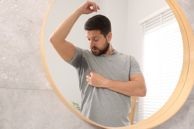 Photo of Emotional man in t-shirt before using deodorant near mirror at home