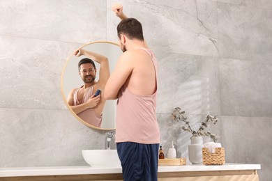 Photo of Smiling man applying roll-on deodorant near mirror at home