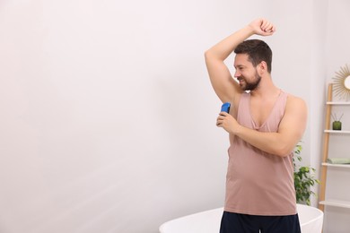 Smiling man applying solid deodorant at home. Space for text