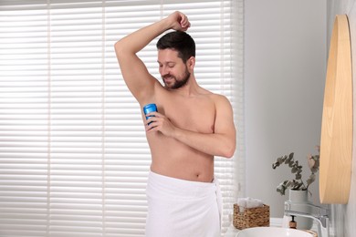 Photo of Smiling man applying solid deodorant in bathroom