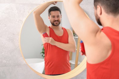 Photo of Smiling man applying solid deodorant near mirror at home