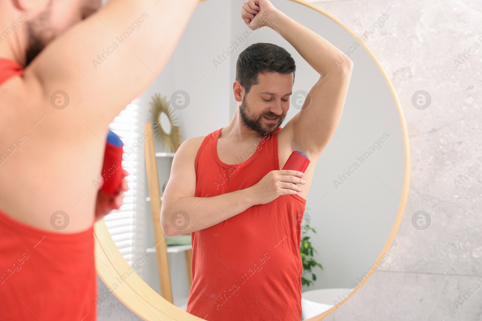 Photo of Smiling man applying solid deodorant near mirror at home