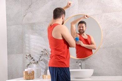 Smiling man applying solid deodorant near mirror at home