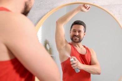 Photo of Smiling man applying spray deodorant near mirror at home