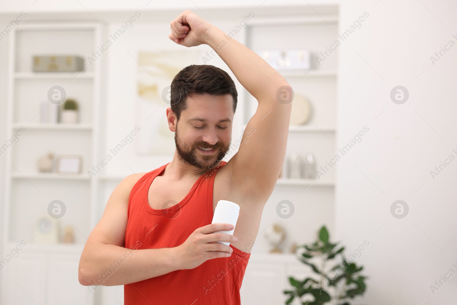 Photo of Smiling man applying solid deodorant at home