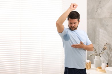 Emotional man in t-shirt before using deodorant at home. Space for text