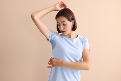 Emotional woman in t-shirt before using deodorant on beige background