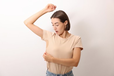 Emotional woman in t-shirt before using deodorant on white background