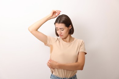 Emotional woman in t-shirt before using deodorant on white background