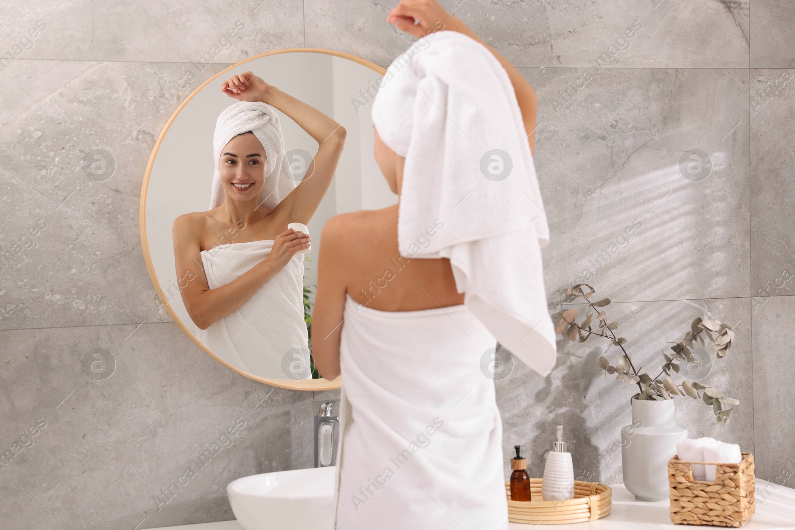 Photo of Smiling woman applying solid deodorant near mirror at home, back view