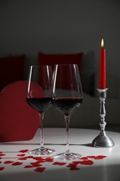 Photo of Burning candle, wine in glasses and paper hearts on table indoors