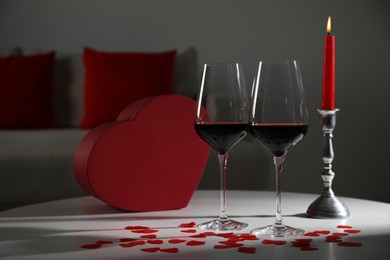 Photo of Burning candle, wine in glasses and paper hearts on table indoors