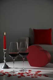 Photo of Burning candle, wine in glasses and paper hearts on table indoors