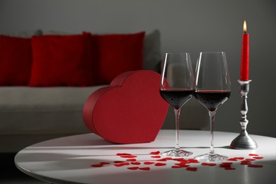 Photo of Burning candle, wine in glasses and paper hearts on table indoors