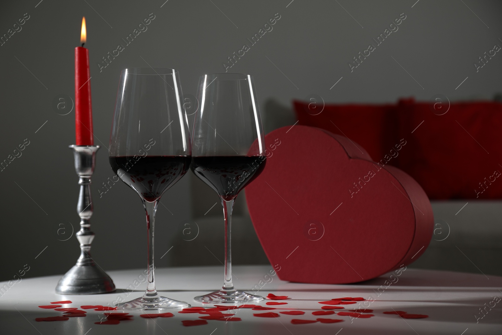 Photo of Burning candle, wine in glasses and paper hearts on table indoors