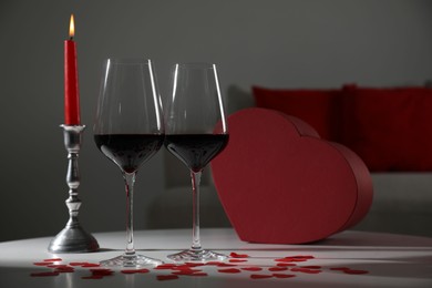 Photo of Burning candle, wine in glasses and paper hearts on table indoors