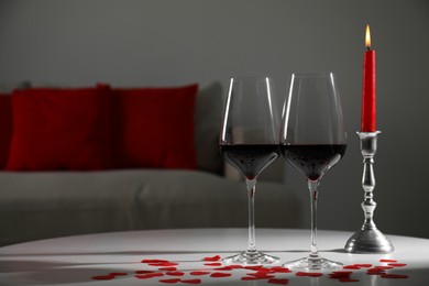 Photo of Burning candle, wine in glasses and paper hearts on table indoors. Space for text