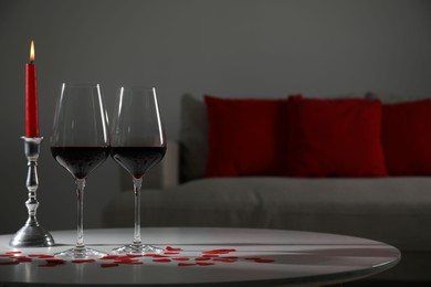 Photo of Burning candle, wine in glasses and paper hearts on table indoors. Space for text